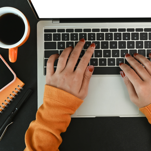 Kvinna skriver på laptop med kaffekopp bredvid