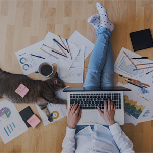 Person som sitter på gulvet med en bærbar datamaskin på fanget. På gulvet er det spredte papirer og