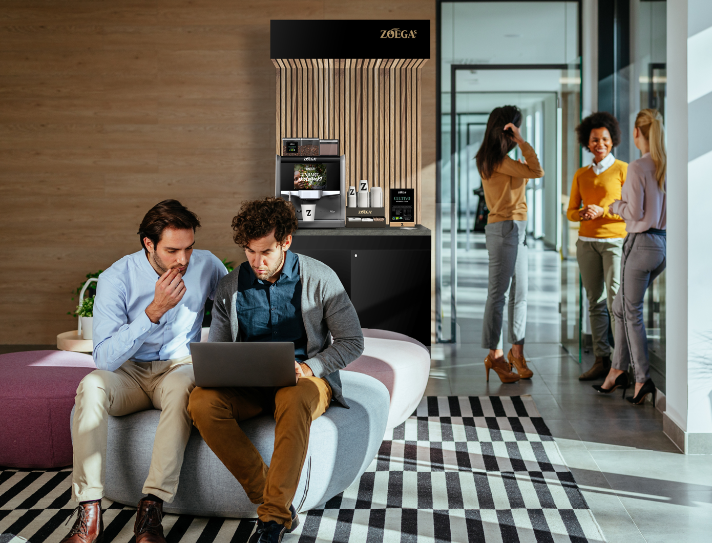 Två kollegor kollar på en laptop med Zoégas kaffemaskin i bakgrunden