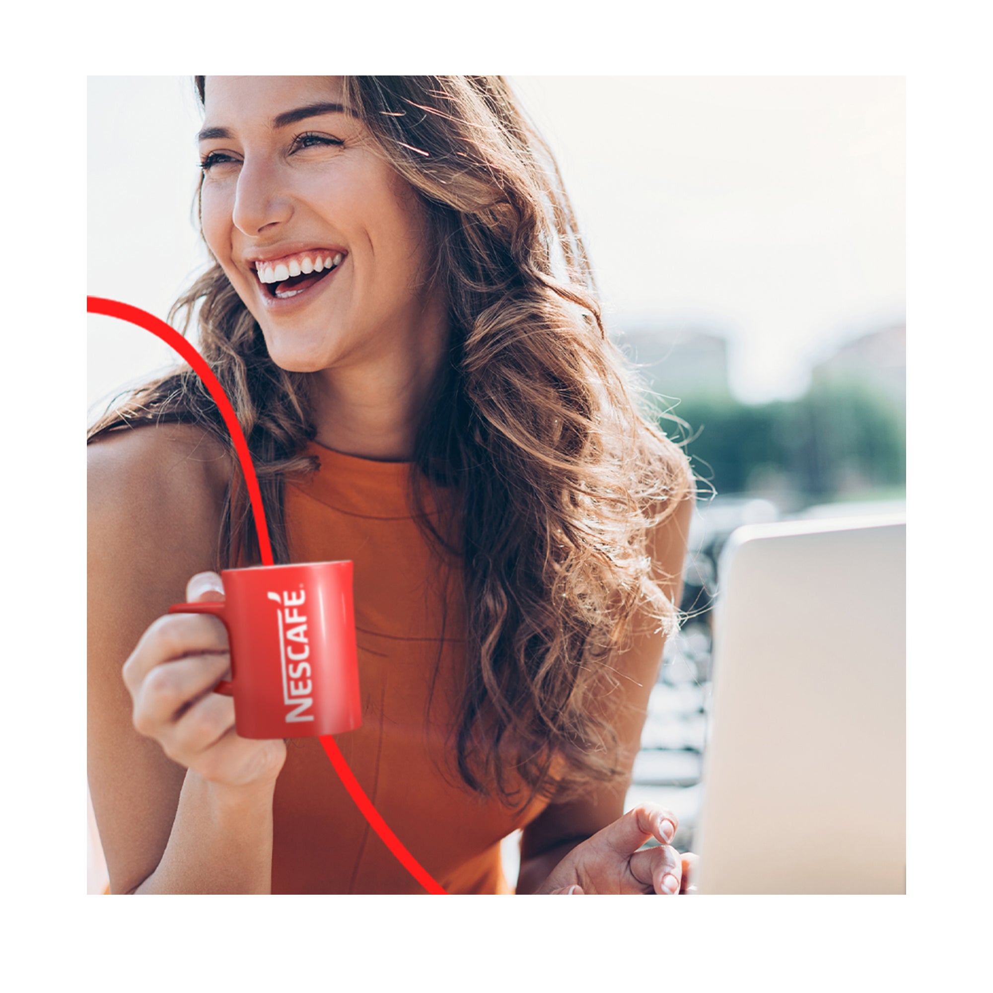 Pitkät hiukset omaava tyttö, jolla on punainen paita, hymyilee ja pitää kädessään punaista Nescafé-kuppia