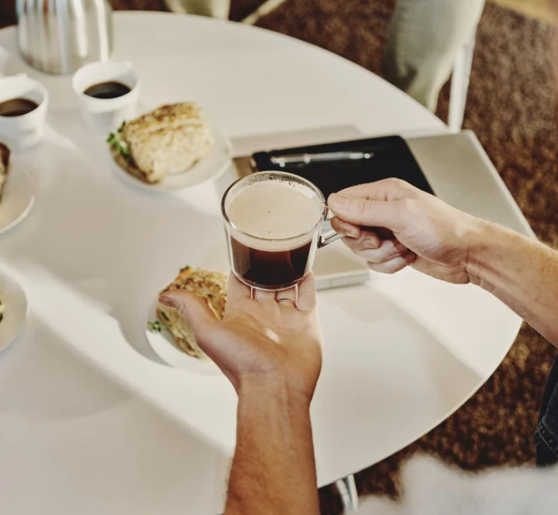 Ett vitt bord med smörgåsar och en person som kommer med kaffe i händerna