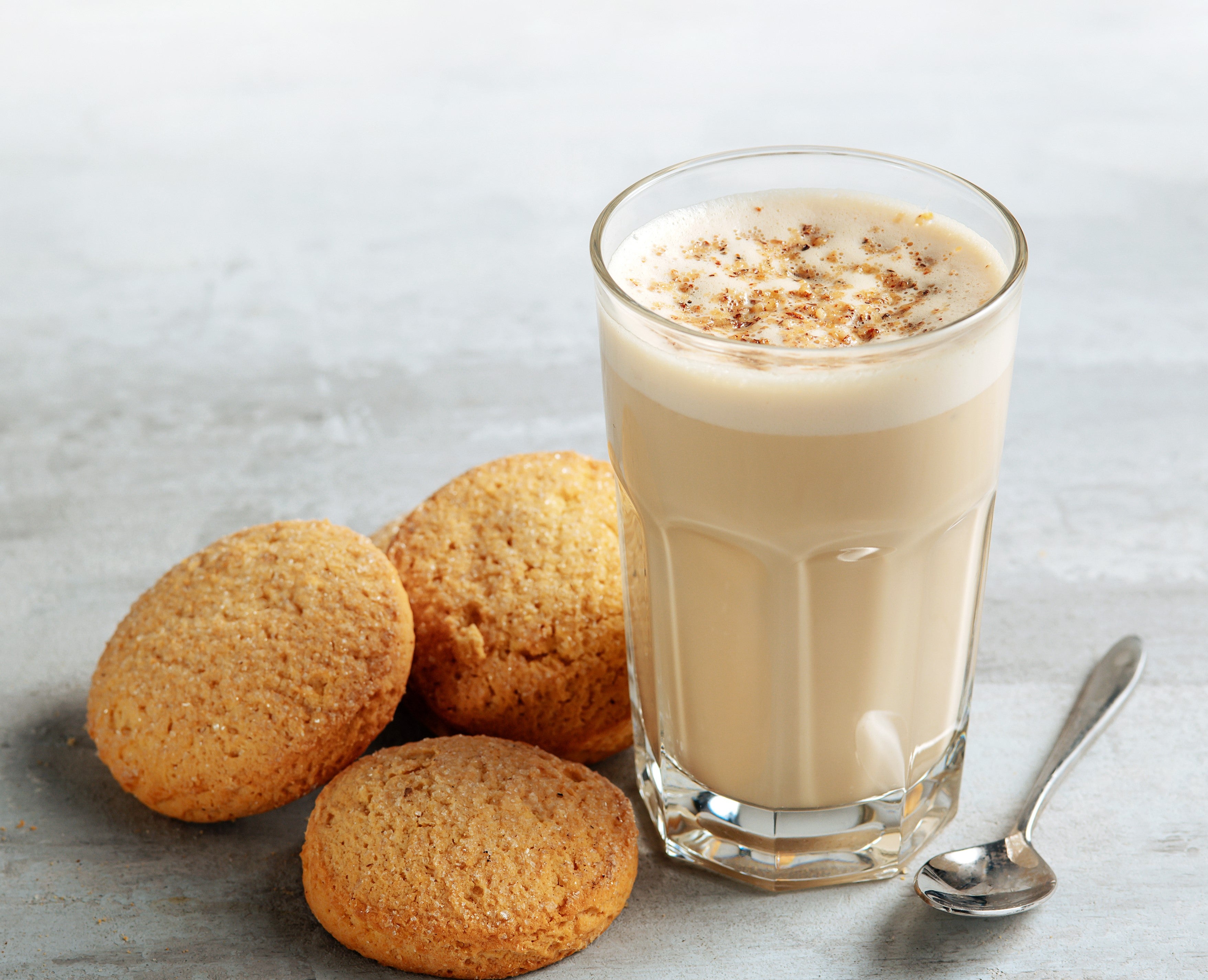 Et glasskopp med kaffe og melk, toppet med noe ekstra og med kjeks ved siden av