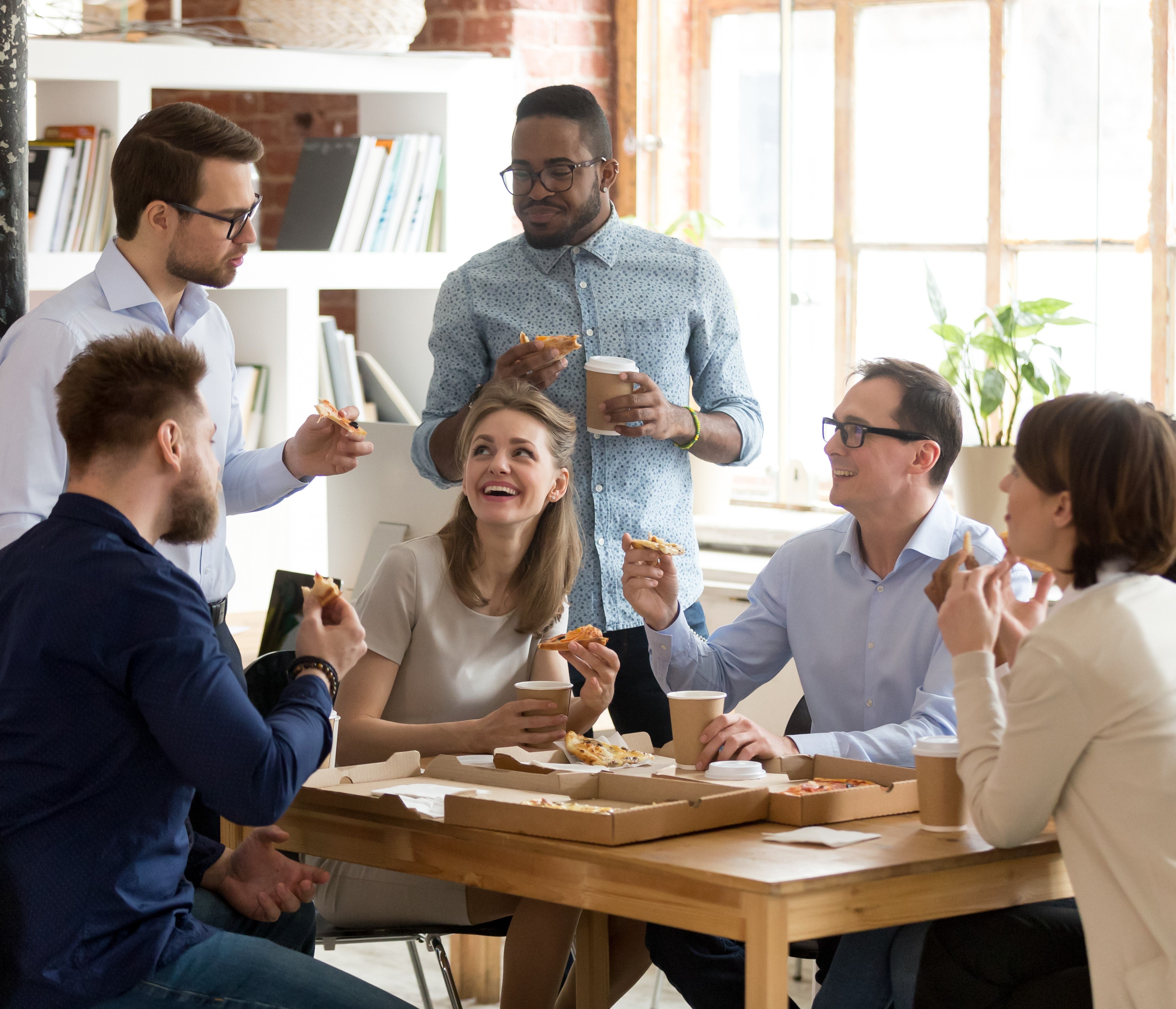 Kollegor äter pizza runt ett matbord