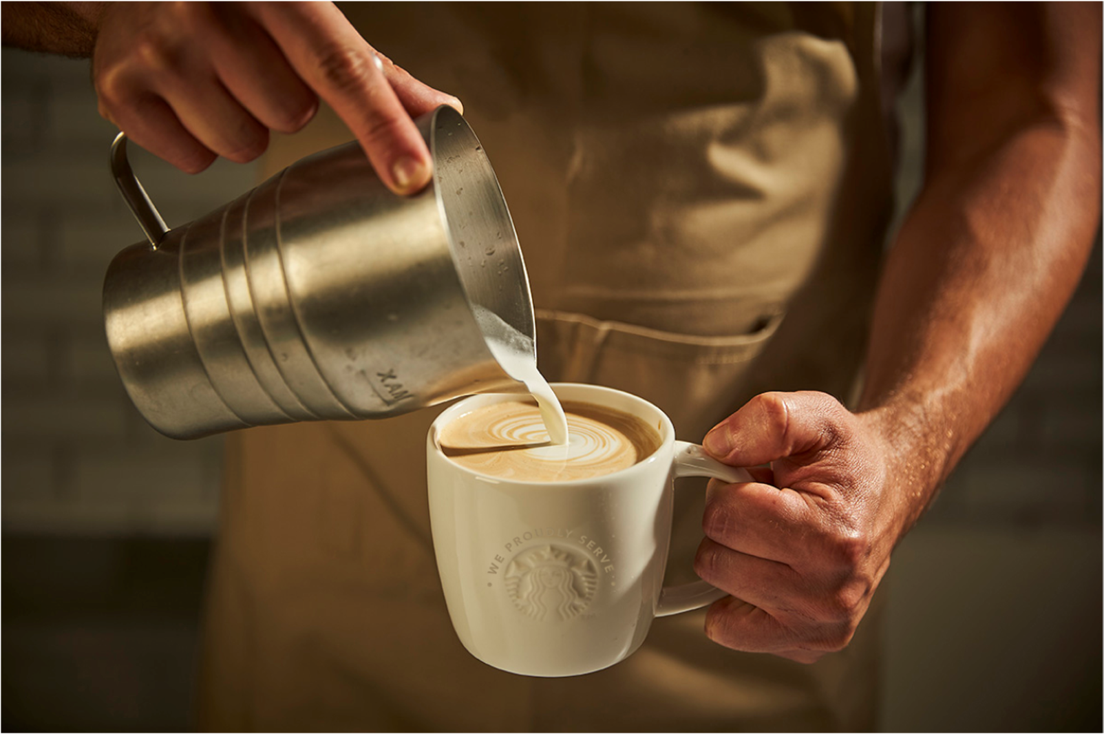 Bartenderen serverer cappuccino i en krus. Vi serverer stolt Starbucks.