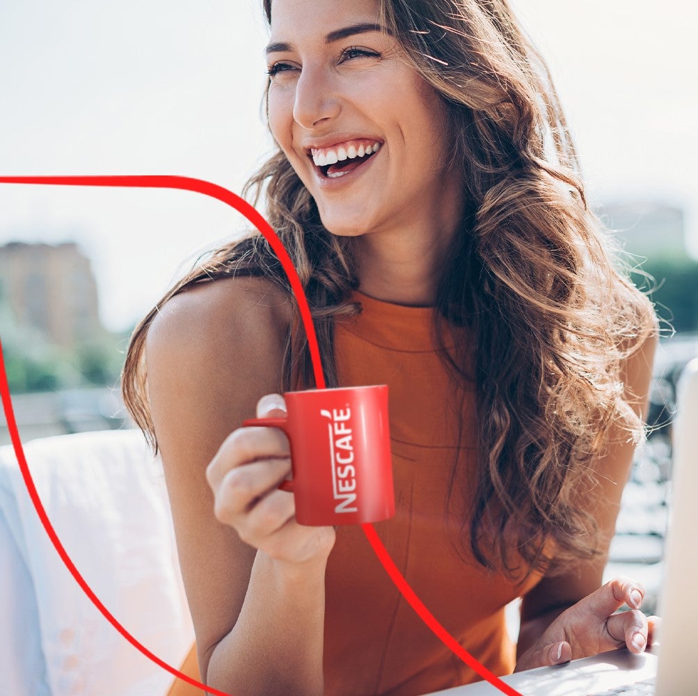 Glad tjej med en röd mugg med Nescafé-logotypen