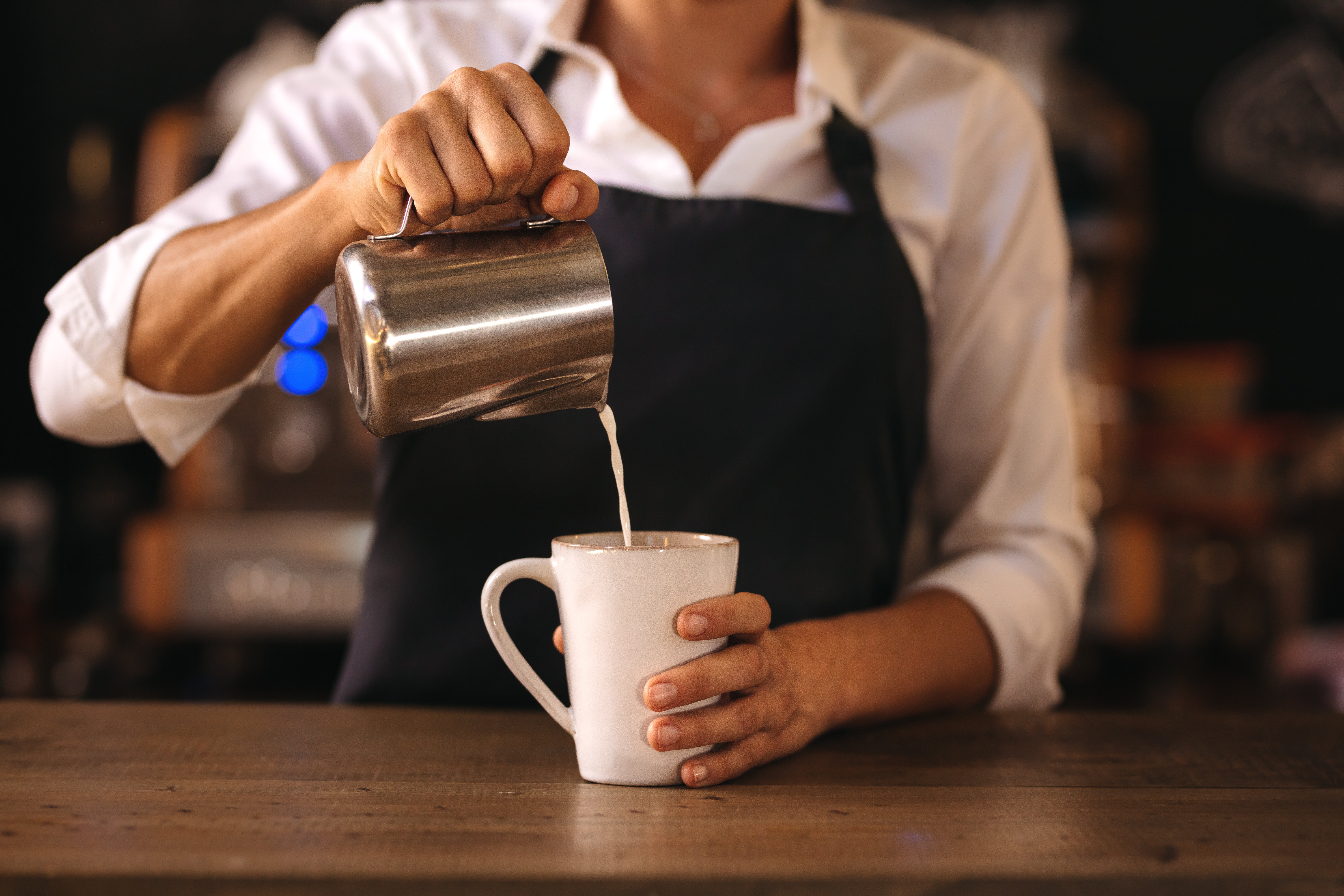 Barista häller mjölk i kopp kaffe