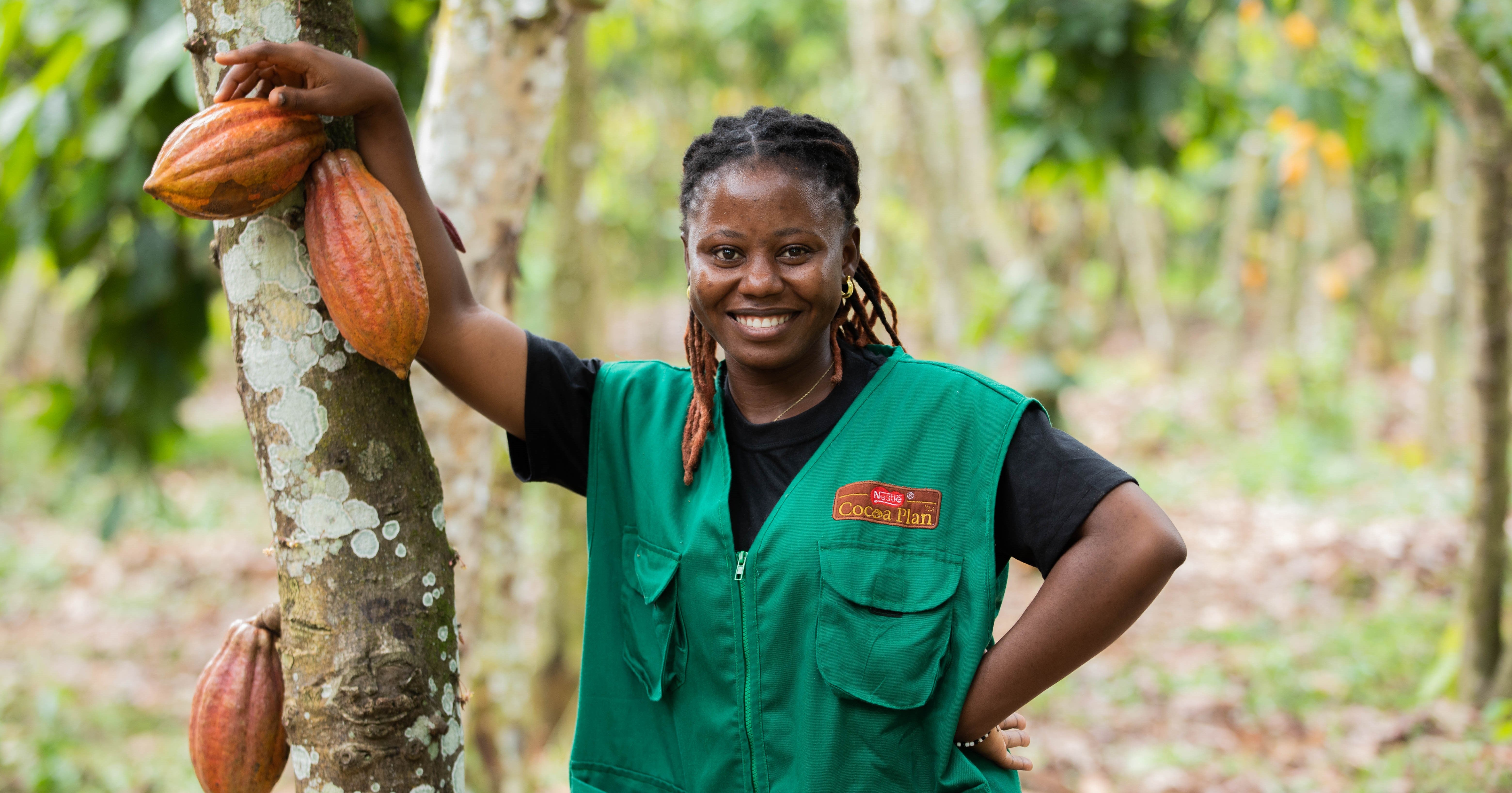 Kvinna står vid ett kakaoträd och ler mot kameran