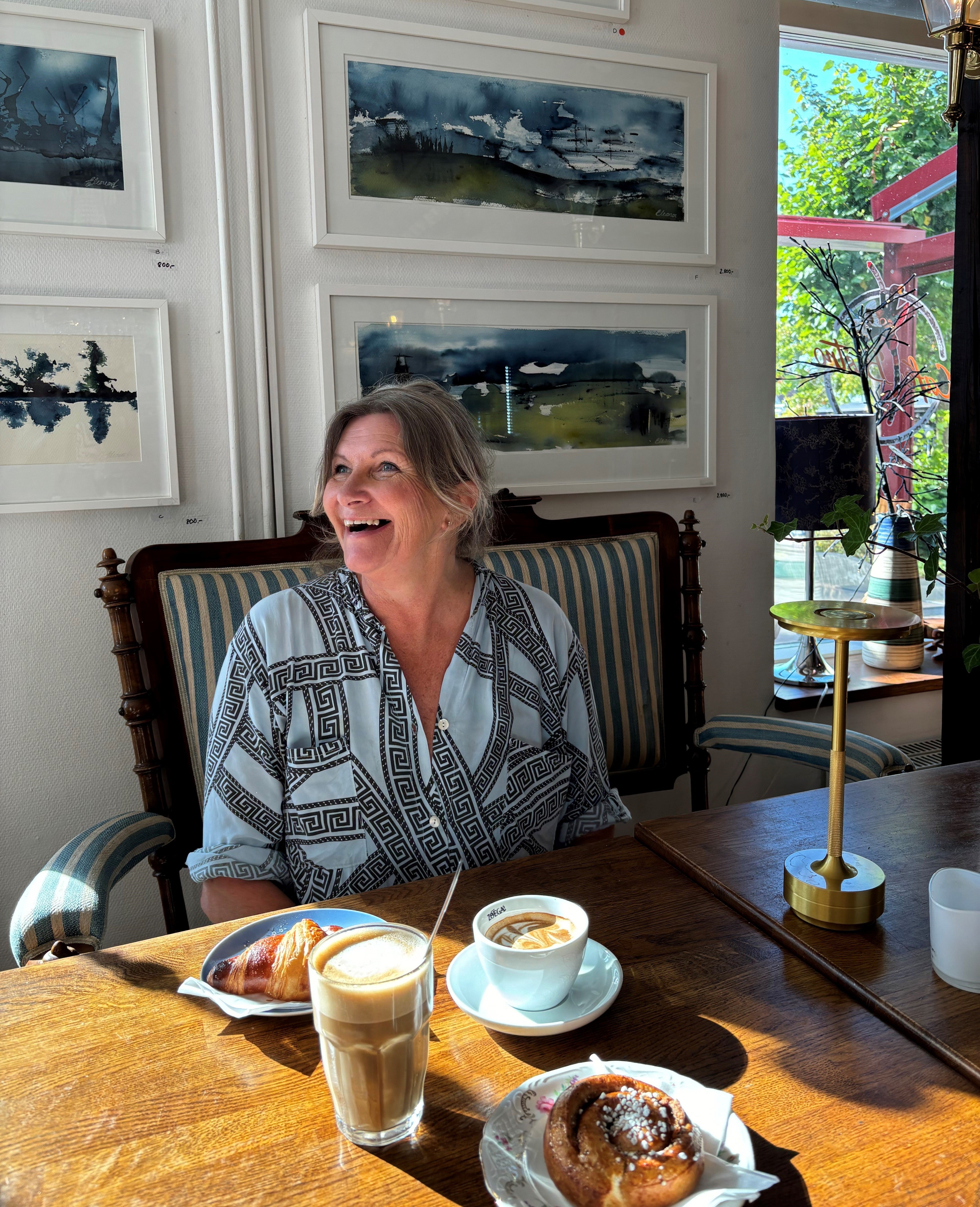 Glad kvinna som sitter vid bordet med kaffe och efterrätter på bordet