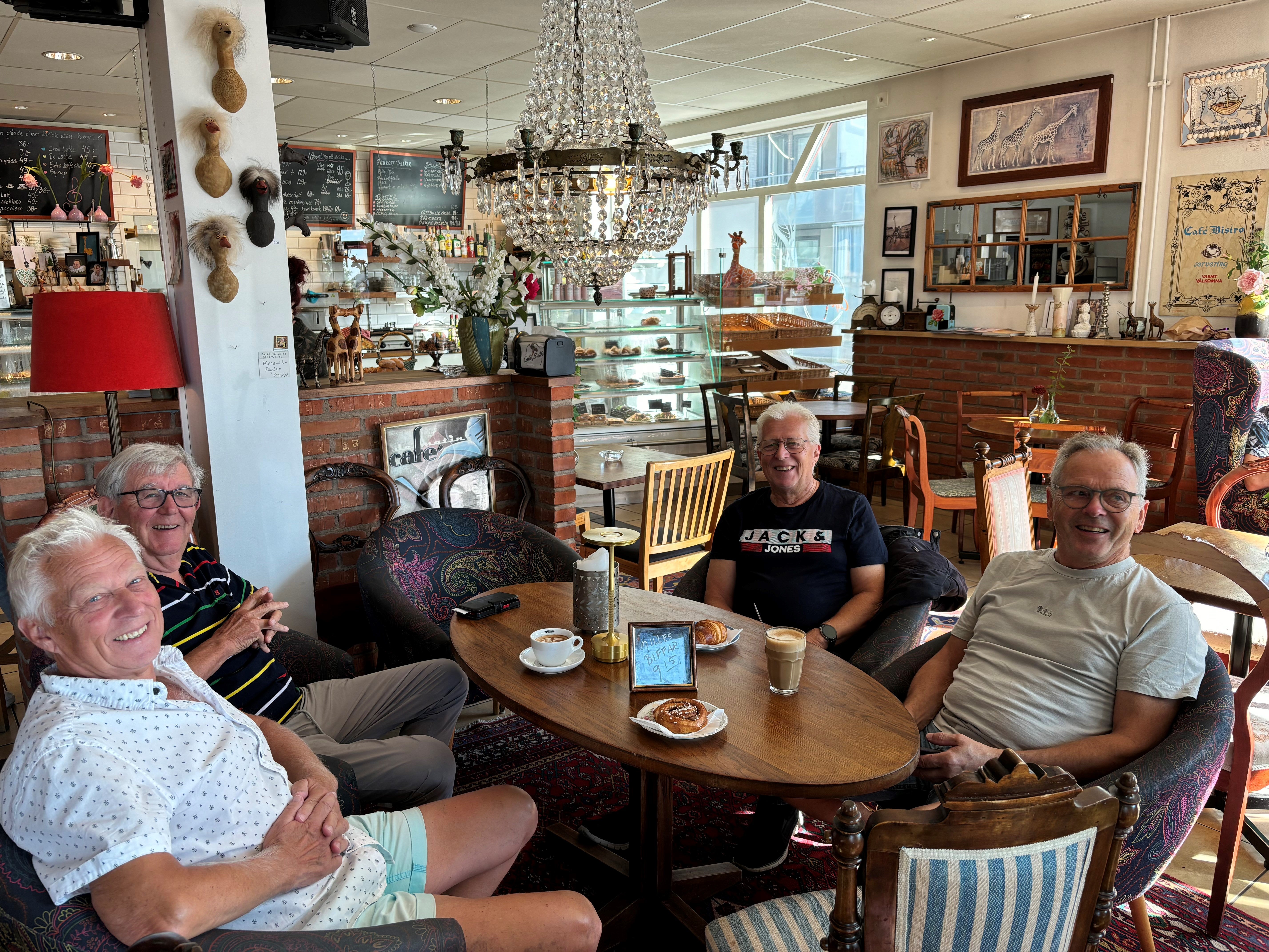 Fyra leende herrar runt ett bord med kaffe och serverade sötsaker