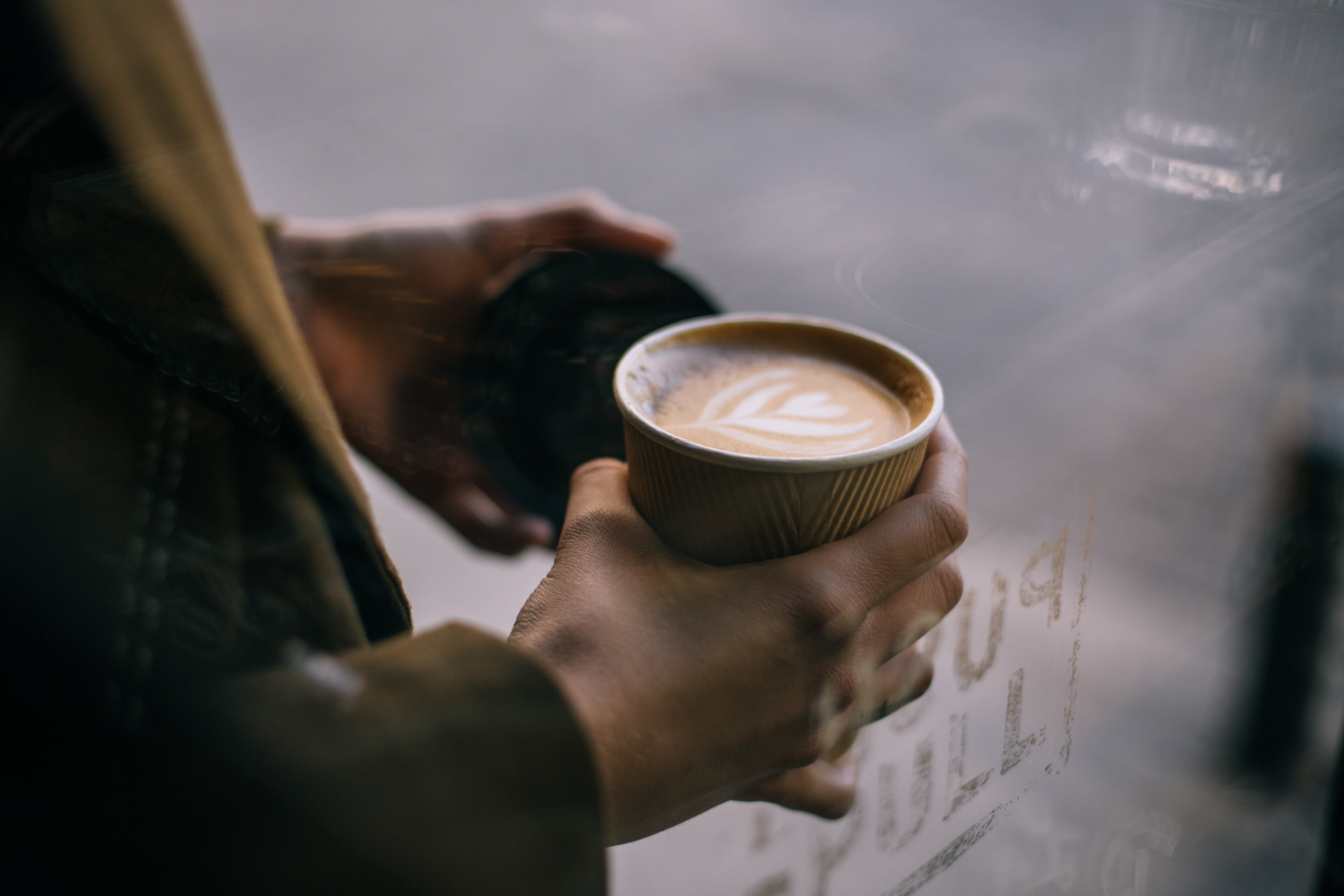 Person med cappuccino i en engångskartongmugg