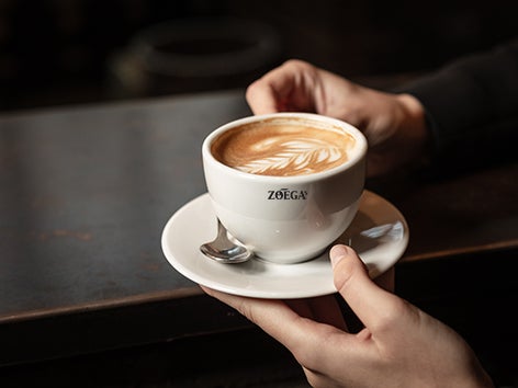 En person som håller en kopp cappuccino i händerna.