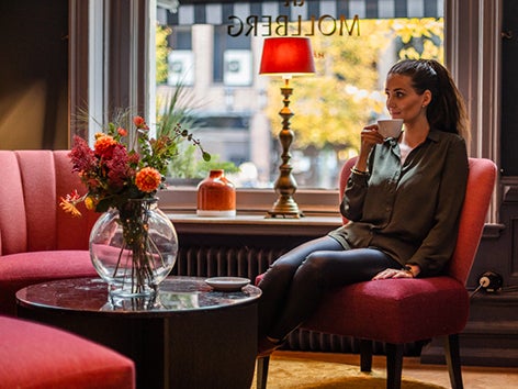 Kvinna som sitter i en fåtölj med en kopp kaffe i handen.