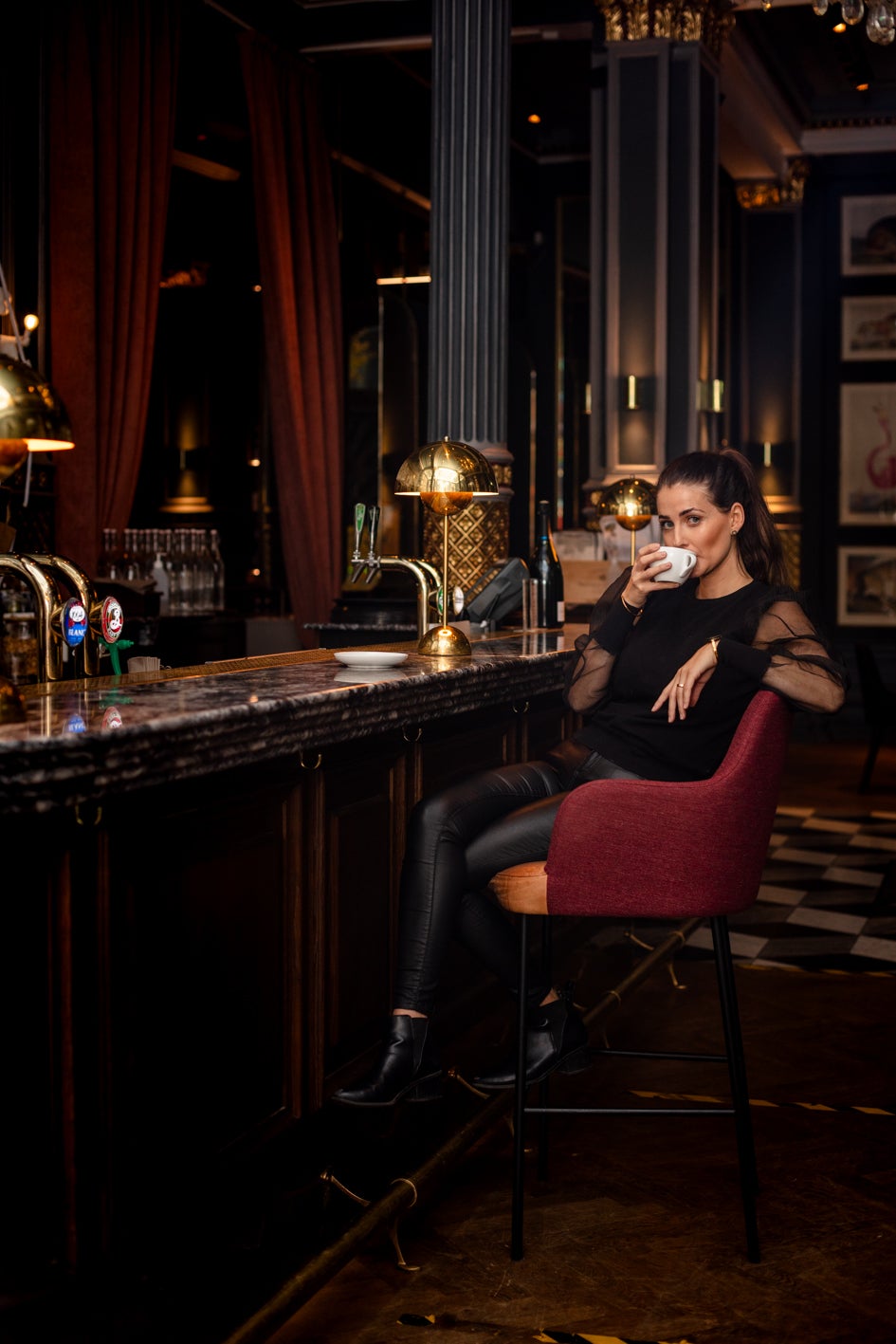 Svartklädd flicka sitter på en hög stol i en bar och njuter av sitt kaffe
