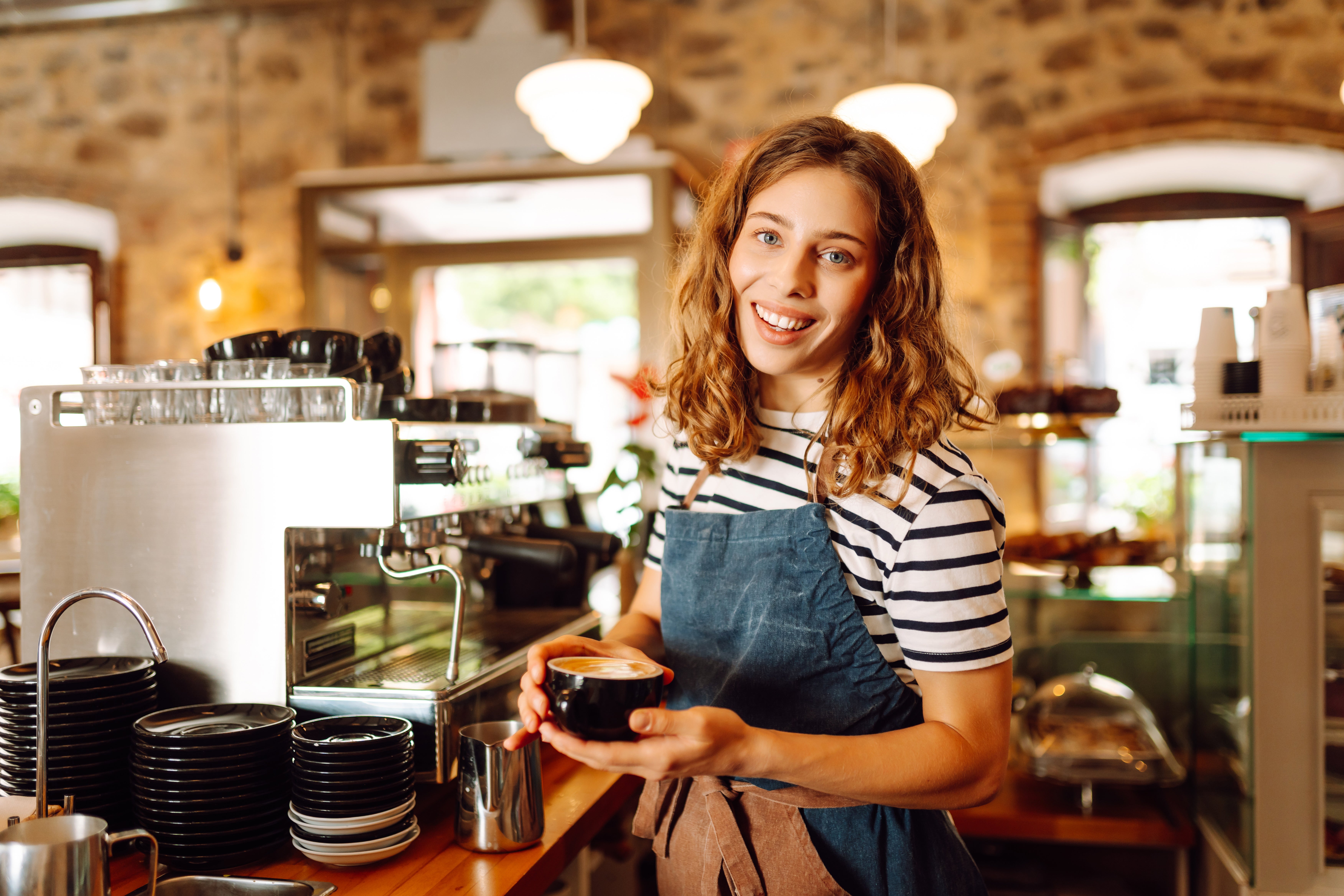 kvinna vid espressomaskin med cappuccino i hand
