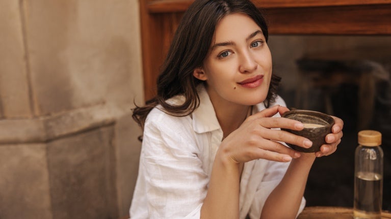 En tjej som sitter med en kopp kaffe i handen i en pose för att bli fotograferad.
