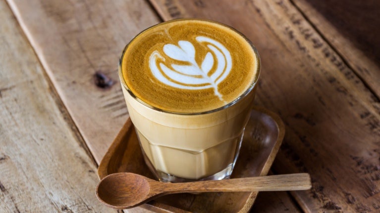 Ett glas med latte på träbricka