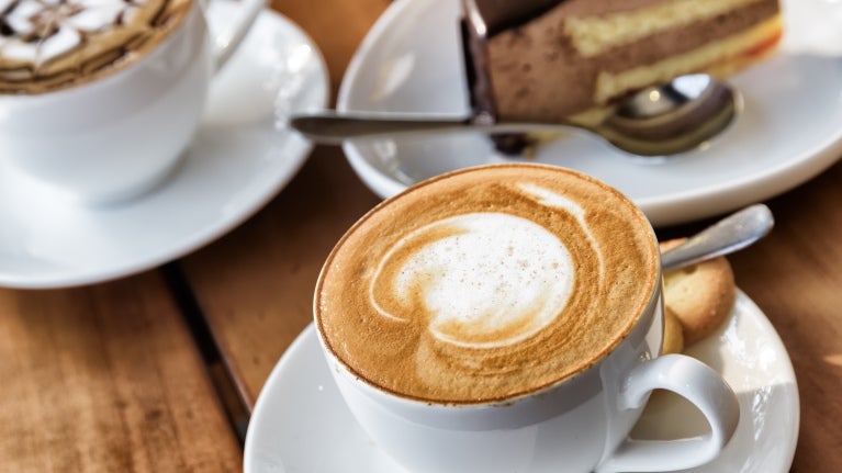 Cappuccino på ett bord tillsammans med fler kaffekoppar och efterrätt