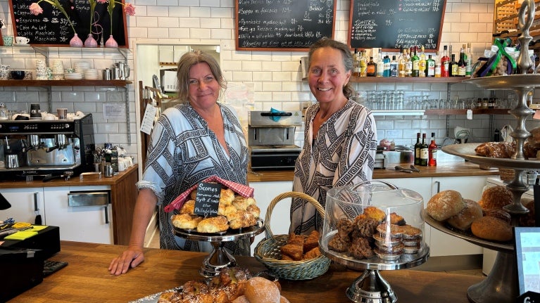 Kvinna som sitter vid bordet med en kopp kaffe, croissant och en bit tårta
