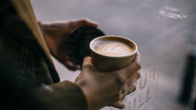 Person med cappuccino i en engångskartongmugg