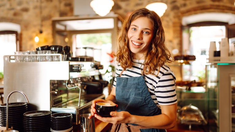 kvinna vid espressomaskin med cappuccino i hand