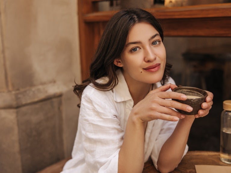 En tjej som sitter med en kopp kaffe i handen i en pose för att bli fotograferad.