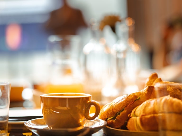 Ett bord med en tallrik med croissanter, en kaffekopp och ett glas vatten.