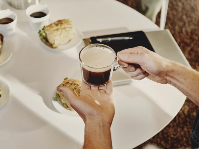 Ett vitt bord med smörgåsar och en person som kommer med kaffe i händerna