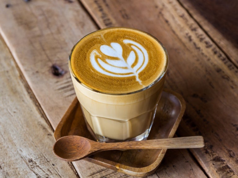 Ett glas med latte på träbricka