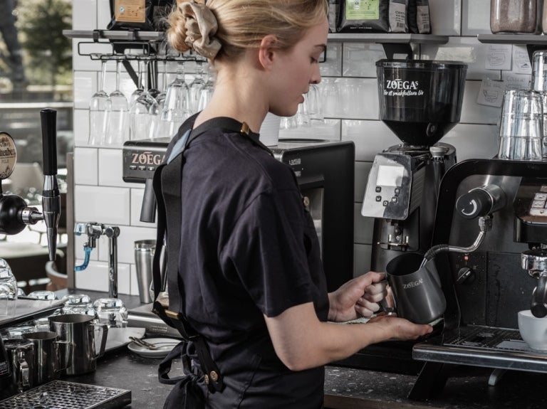 Blond tjej som arbetar inom restaurangbranschen och brygger Zoégas-kaffe från en professionell kaffemaskin