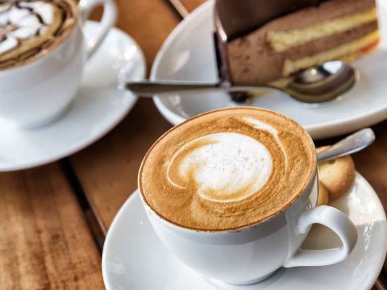Cappuccino på ett bord tillsammans med fler kaffekoppar och efterrätt