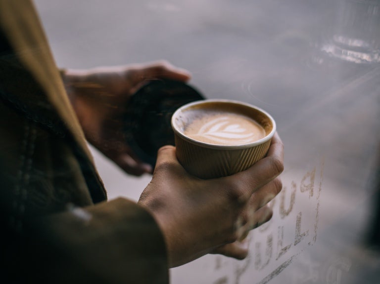 Person med cappuccino i en engångskartongmugg