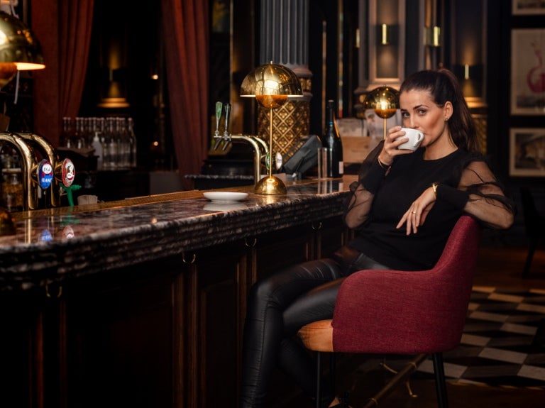 Svartklädd flicka sitter på en hög stol i en bar och njuter av sitt kaffe