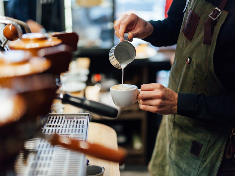 barista vid espressomaskin häller cappuccino