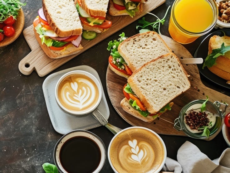 Ett bord sedd uppifrån med tallrikar med smörgåsar, cappuccinos, kaffe och apelsinjuice