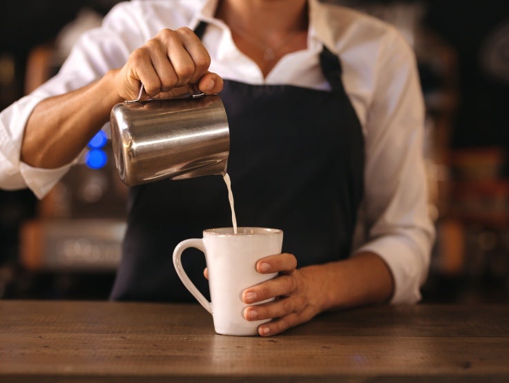 Barista häller mjölk i kopp kaffe