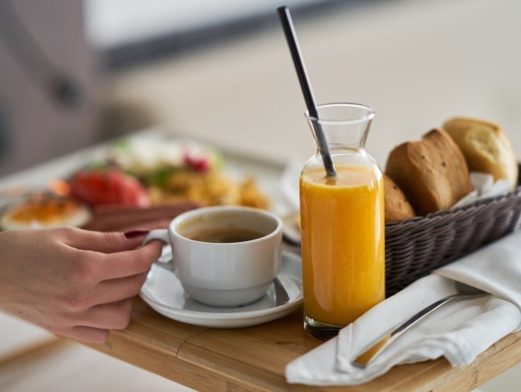 Bricka med kaffe, apelsinjuice, bakverk och frukt.