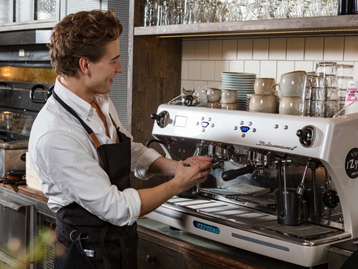 Kaféanställd som arbetar vid en professionell kaffemaskin.