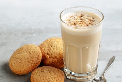 Et glasskopp med kaffe og melk, toppet med noe ekstra og med kjeks ved siden av