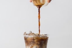 Henkilö kaataa kahvia läpinäkyvään lasiin.