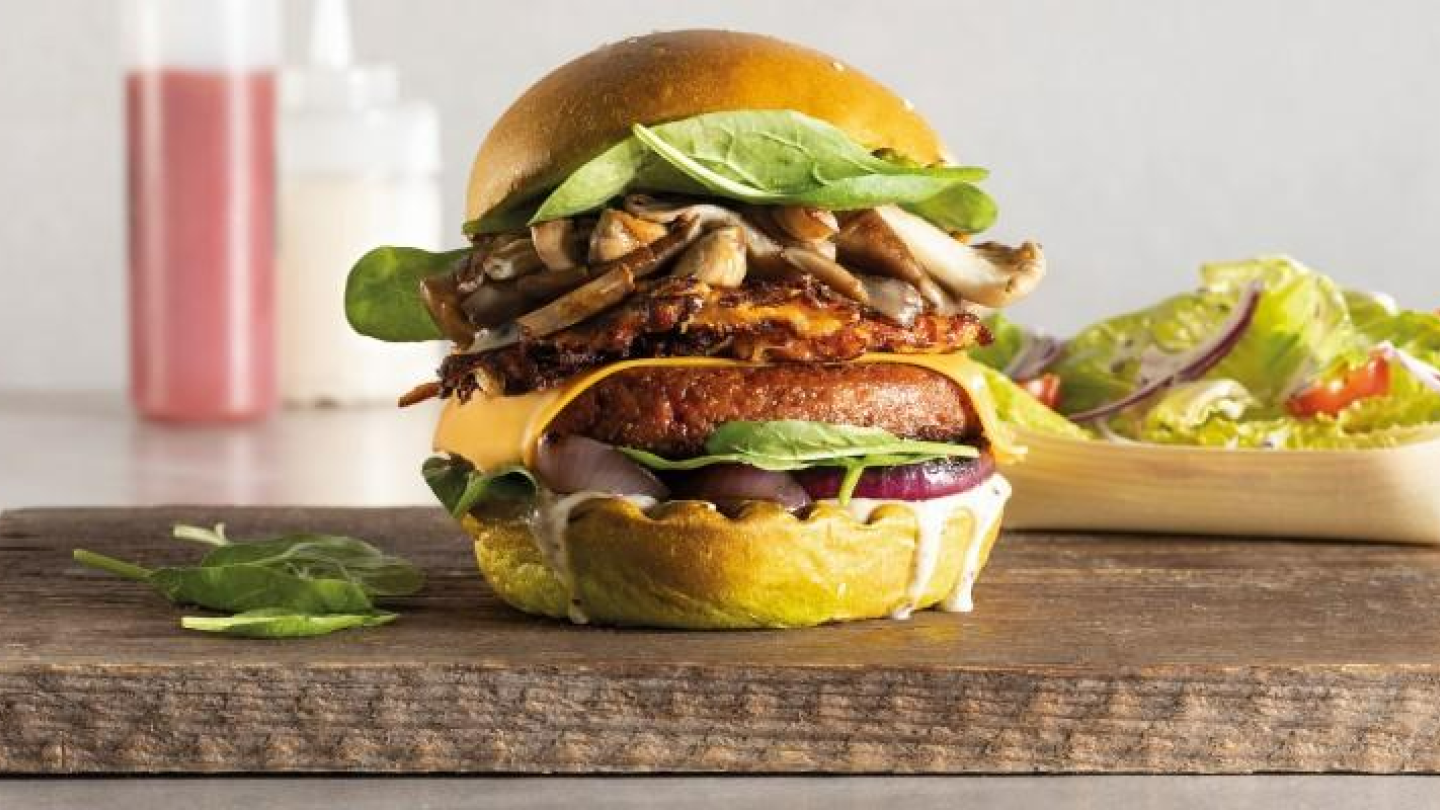 Hamburger serveret på et bræt med saucer i bunden.