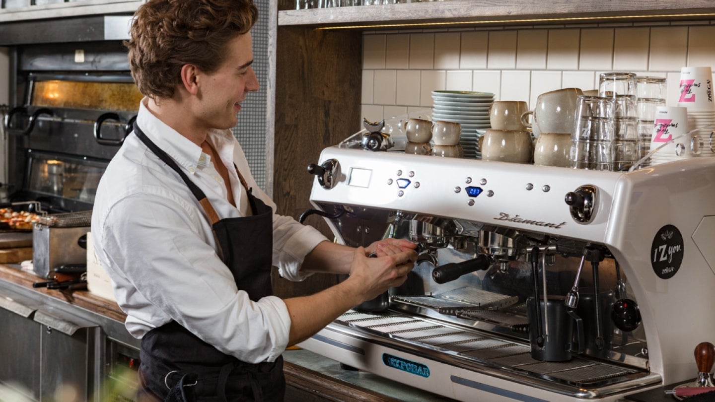Kaféanställd som arbetar vid en professionell kaffemaskin.