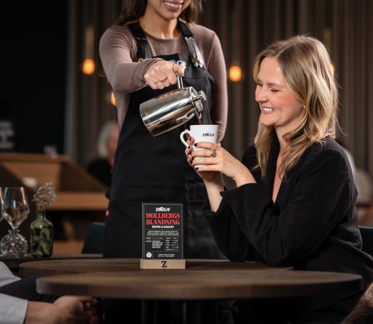 Servitrice hælder kaffe i en kop med Zoégas logo