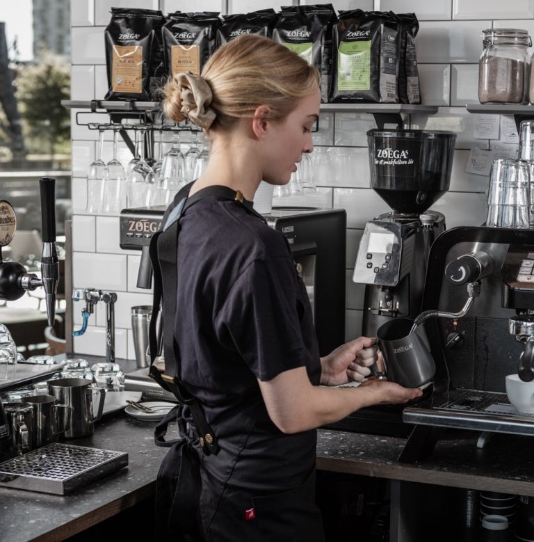 Blond tjej som arbetar inom restaurangbranschen och brygger Zoégas-kaffe från en professionell kaffemaskin