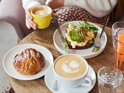 Bord med två kaffekoppar, avokadomacka och croissant.